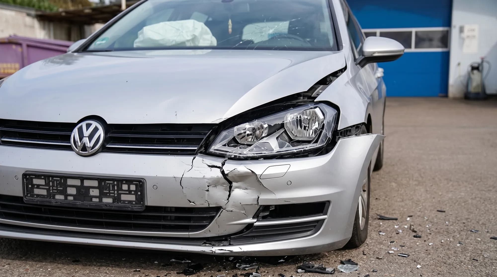 Silberner VW Golf nach einem Unfall auf dem Hof: eine vordere Ecke ist eingedrückt und aufgerissen, der Scheinwerfer zerstört, die Windschutzscheibe gerissen, die Airbags im Innenraum sind ausgelöst